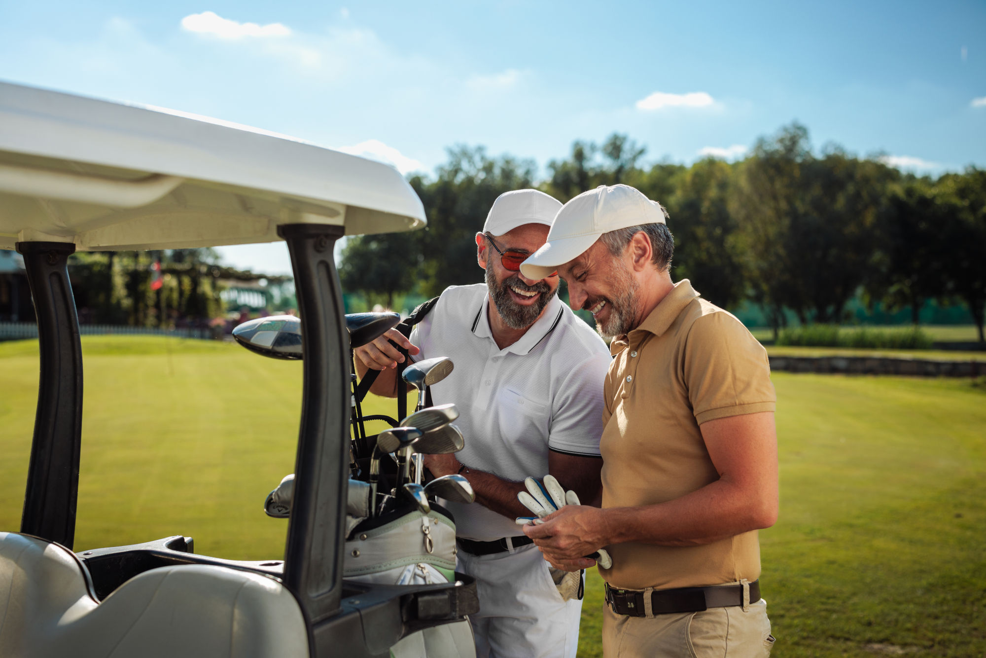 Two friends laughing by the golf cart on the field